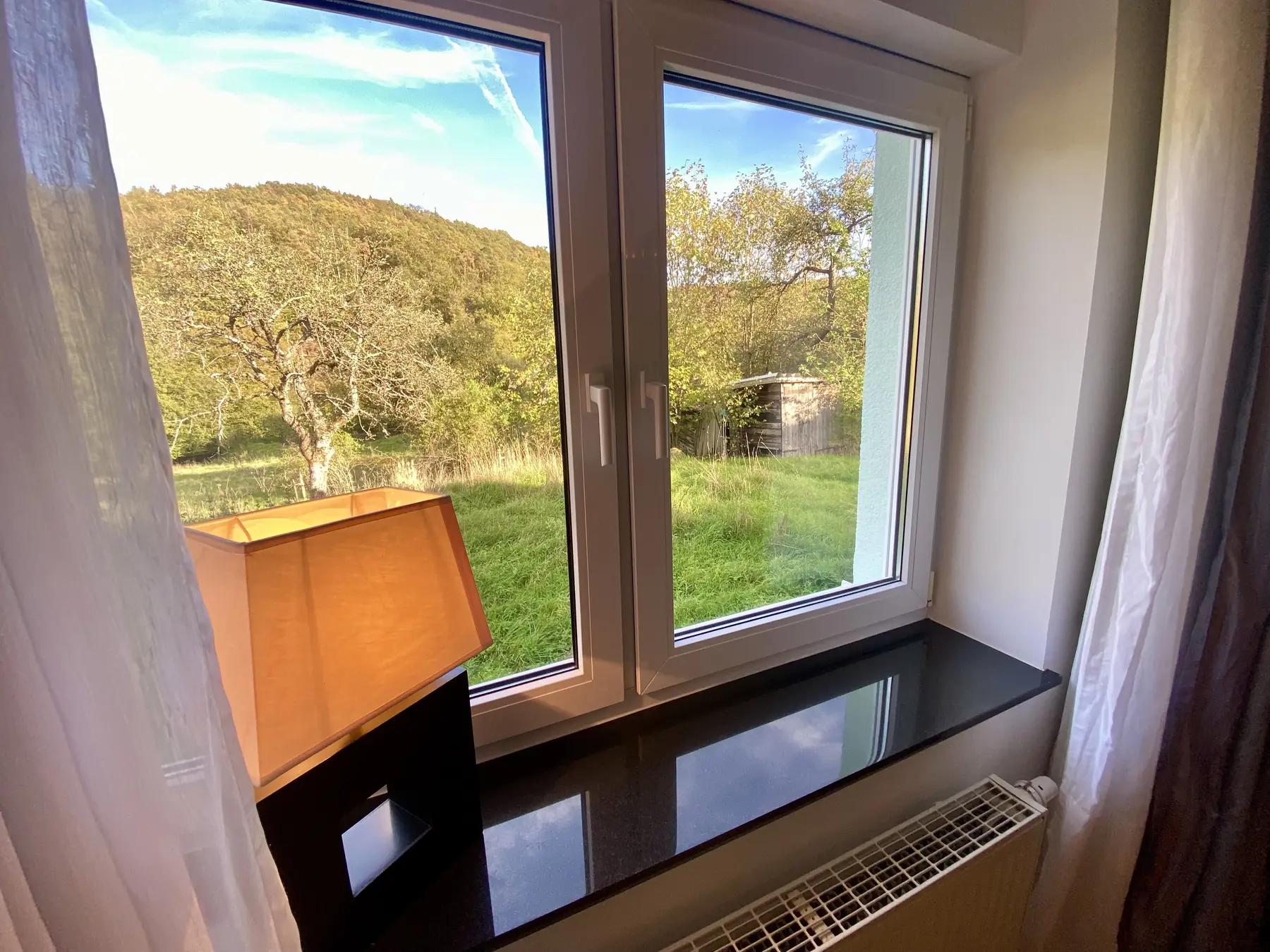 Blick aus dem Fenster auf Wald, Wiese und ein kleines Gartenhäuschen