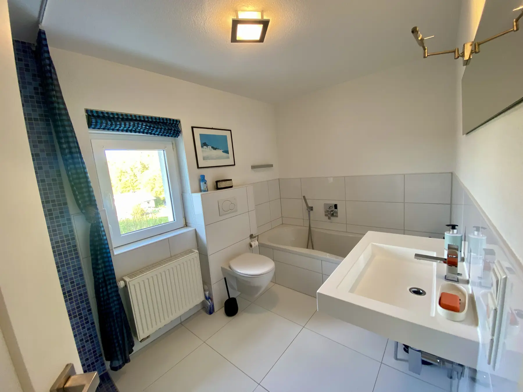 Das Bad mit Badewanne, WC und Mosaikfliesen am Fenster