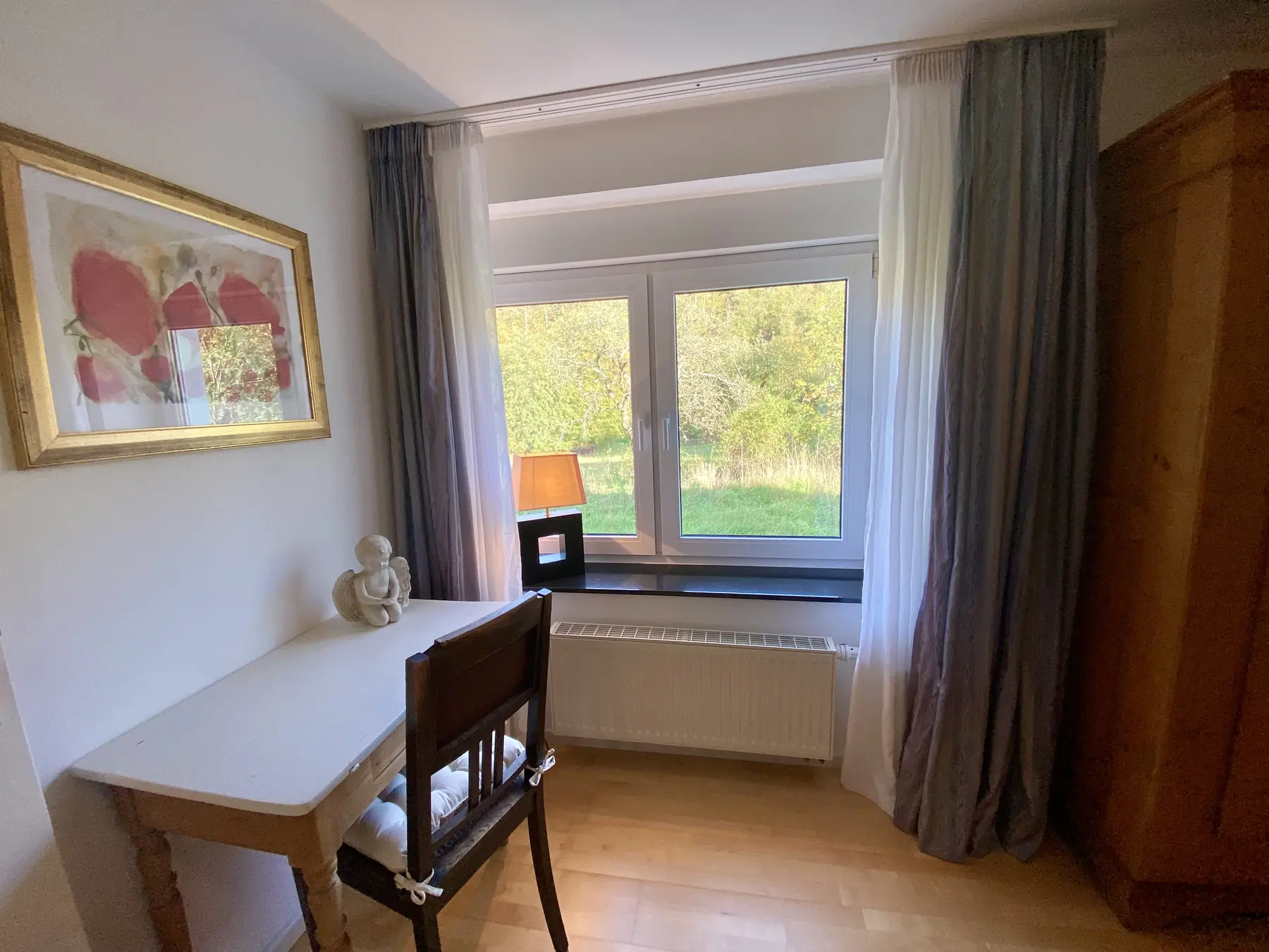 Schreibtisch am Fenster mit Blick auf Wiese und Bäume